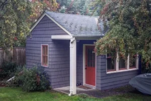 A gray ADU with a red door surrounded by folliage